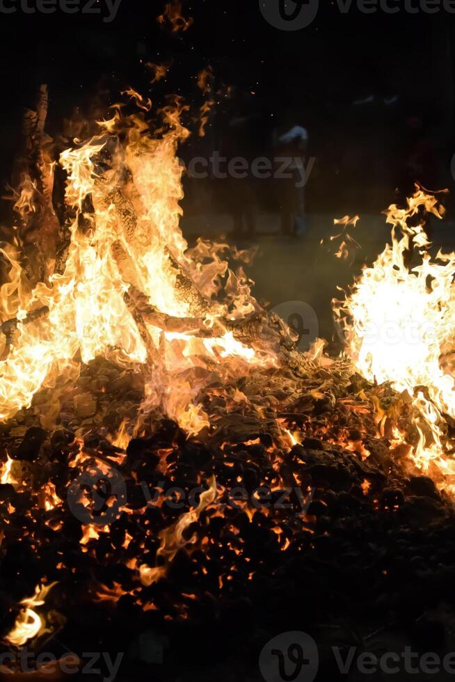 A bonfire is lit up with flames and people standing around photo