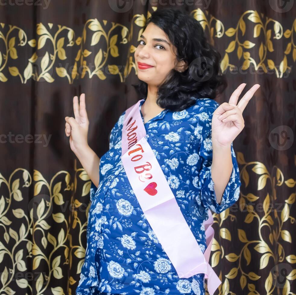A pregnant woman poses for a photo with a sash