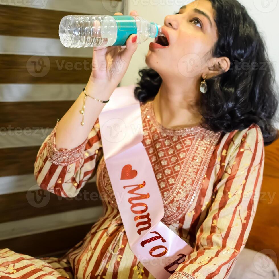 A woman drinking water from a bottle while sitting on a bed photo