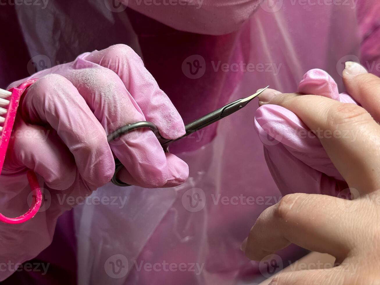 Close up of manicure process with cuticle nipper and pink gloves photo