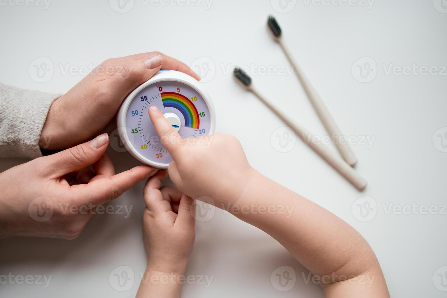 Caucasian female and child setting timer with toothbrushes nearby on white background photo