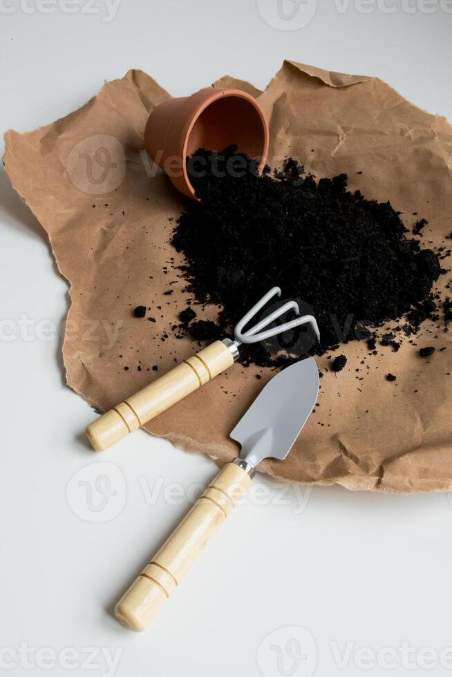 Brown paper with spilled soil and gardening tools on white background photo