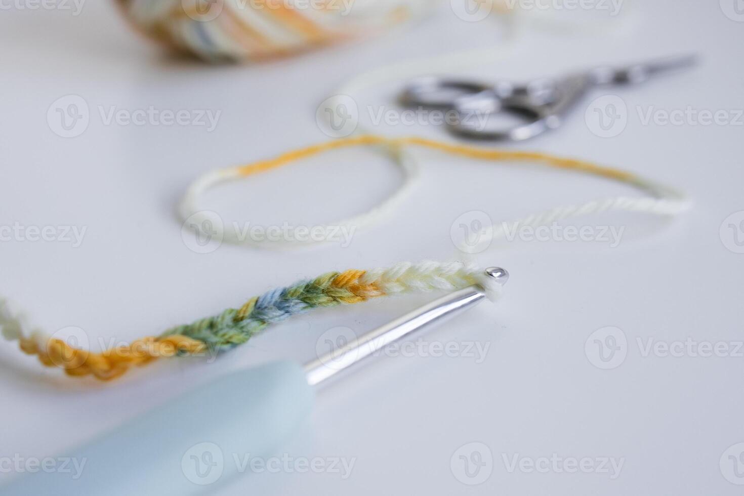 Colorful crocheting yarn with hook and scissors on white surface photo