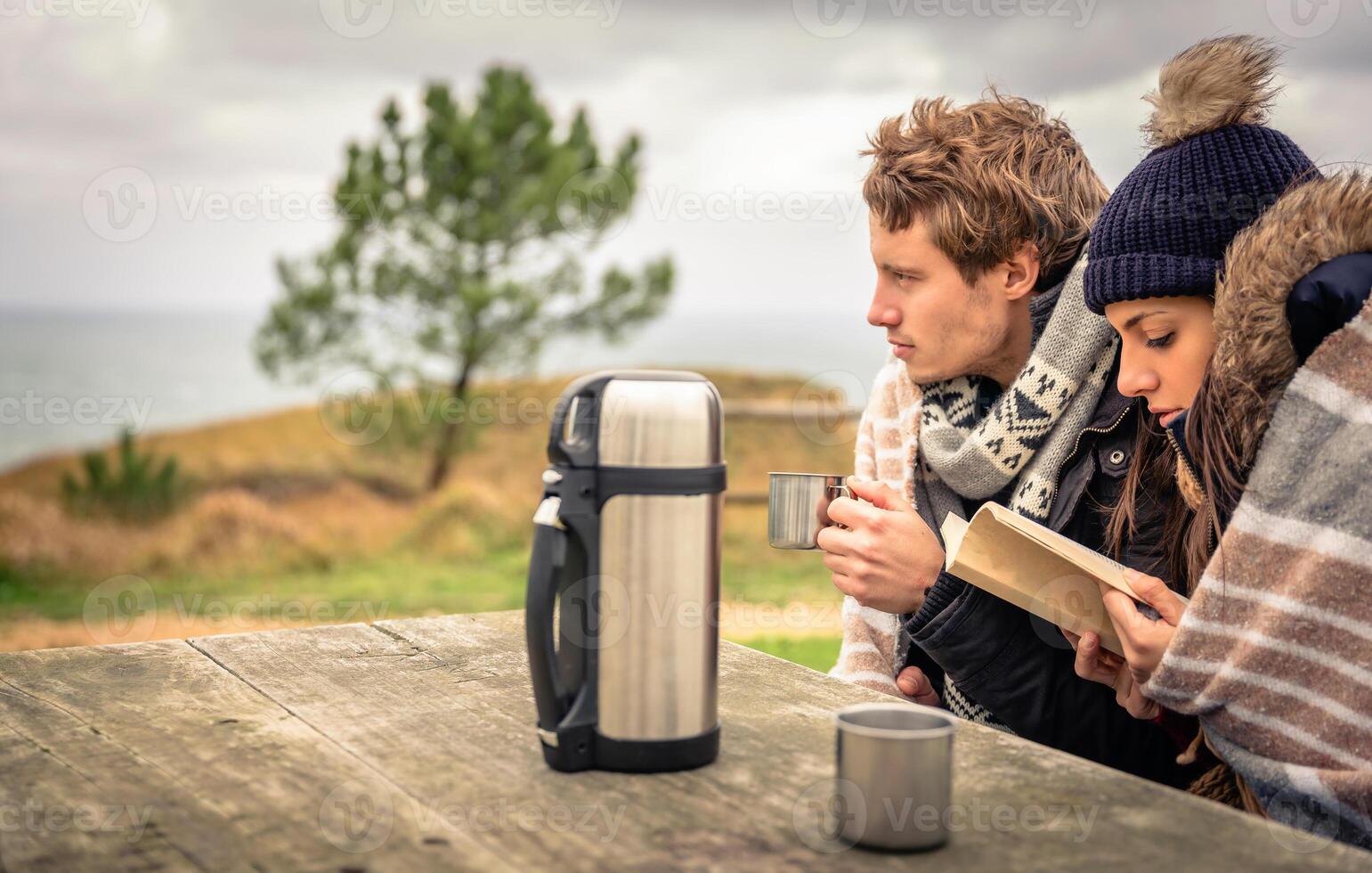 A man and woman sitting at a picnic table with a book and coffee photo