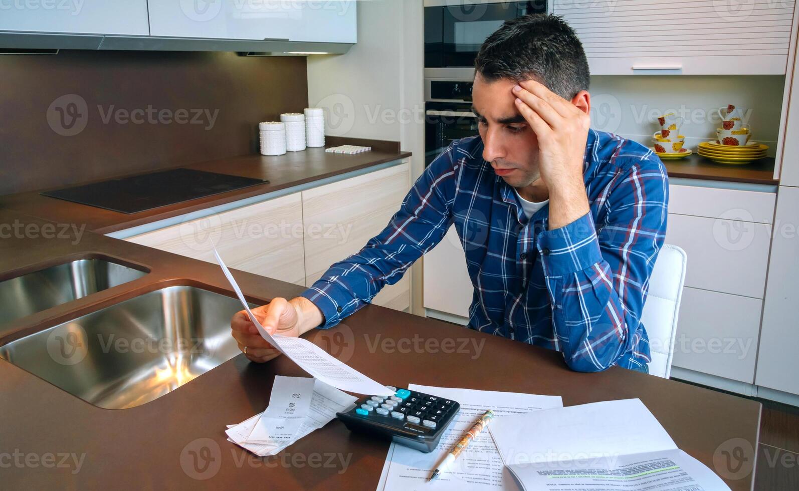 Man with calculator and papers in kitchen. photo