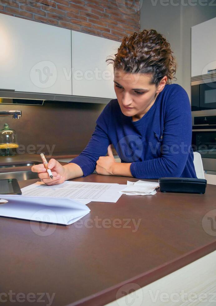 A woman writing on a piece of paper while sitting at a kitchen table photo