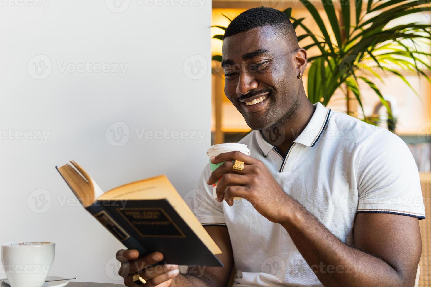 A smiling man is reading a book while sitting at a table photo