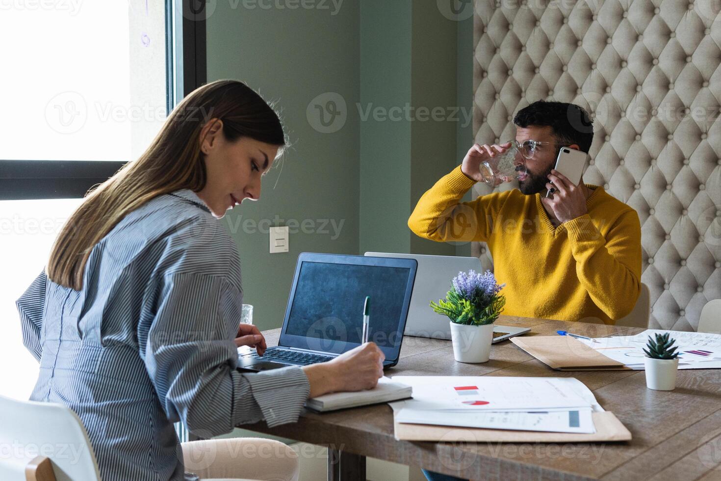 A man is drinking water and woman sitting at a table with laptop photo