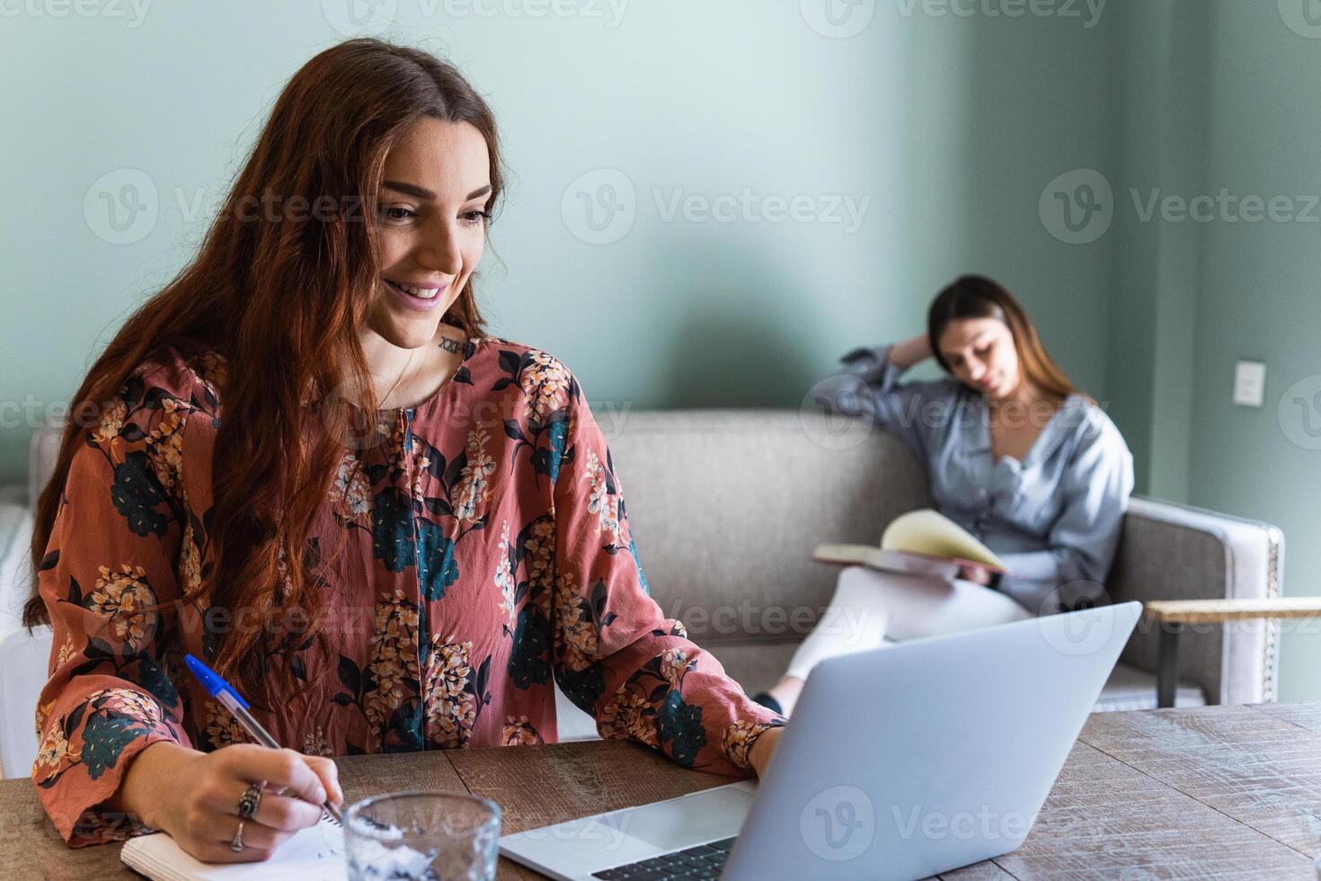 A woman sitting at a table with a laptop and a pen to write down a note. photo