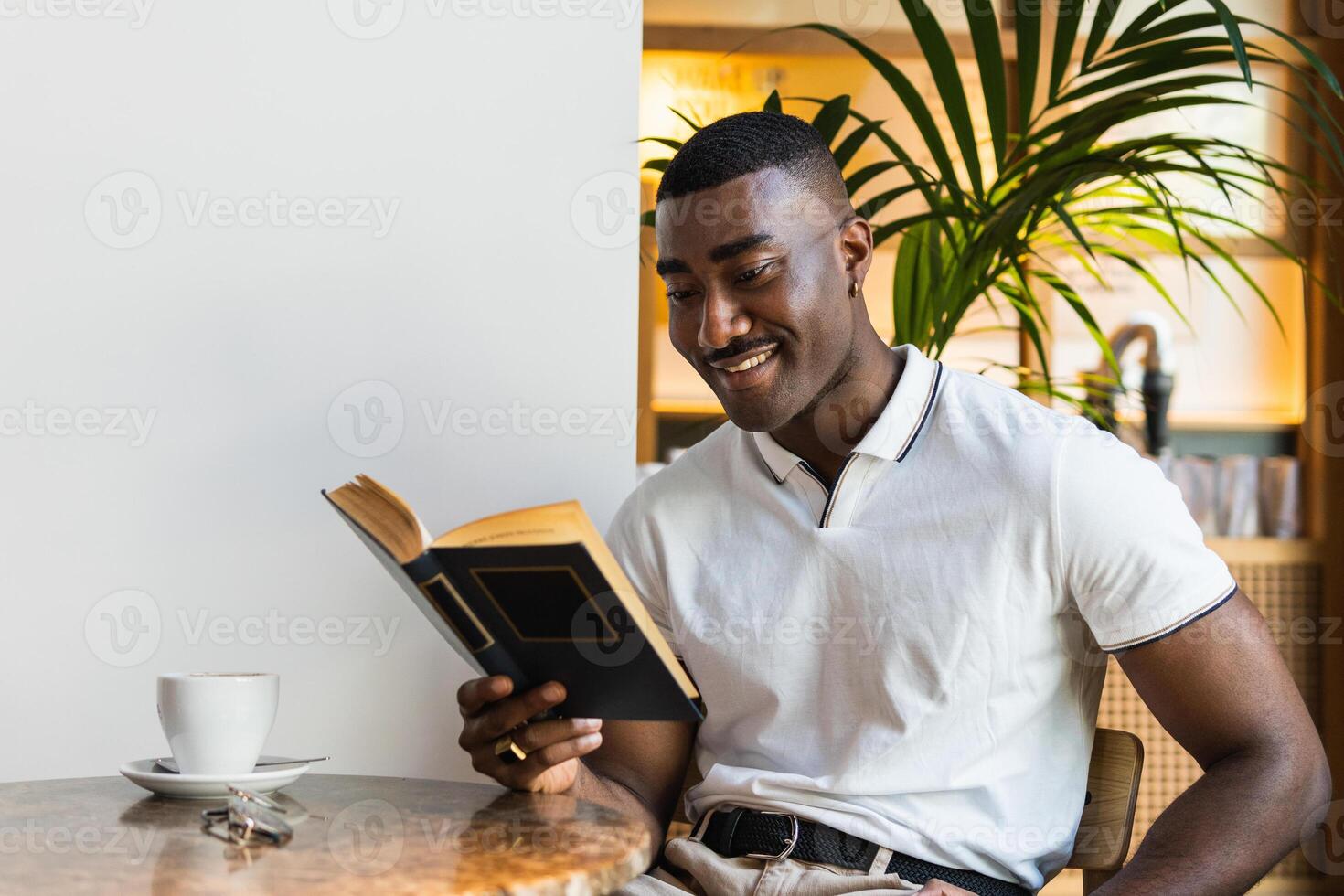 A smiling adult man is reading a book while sitting at a table photo