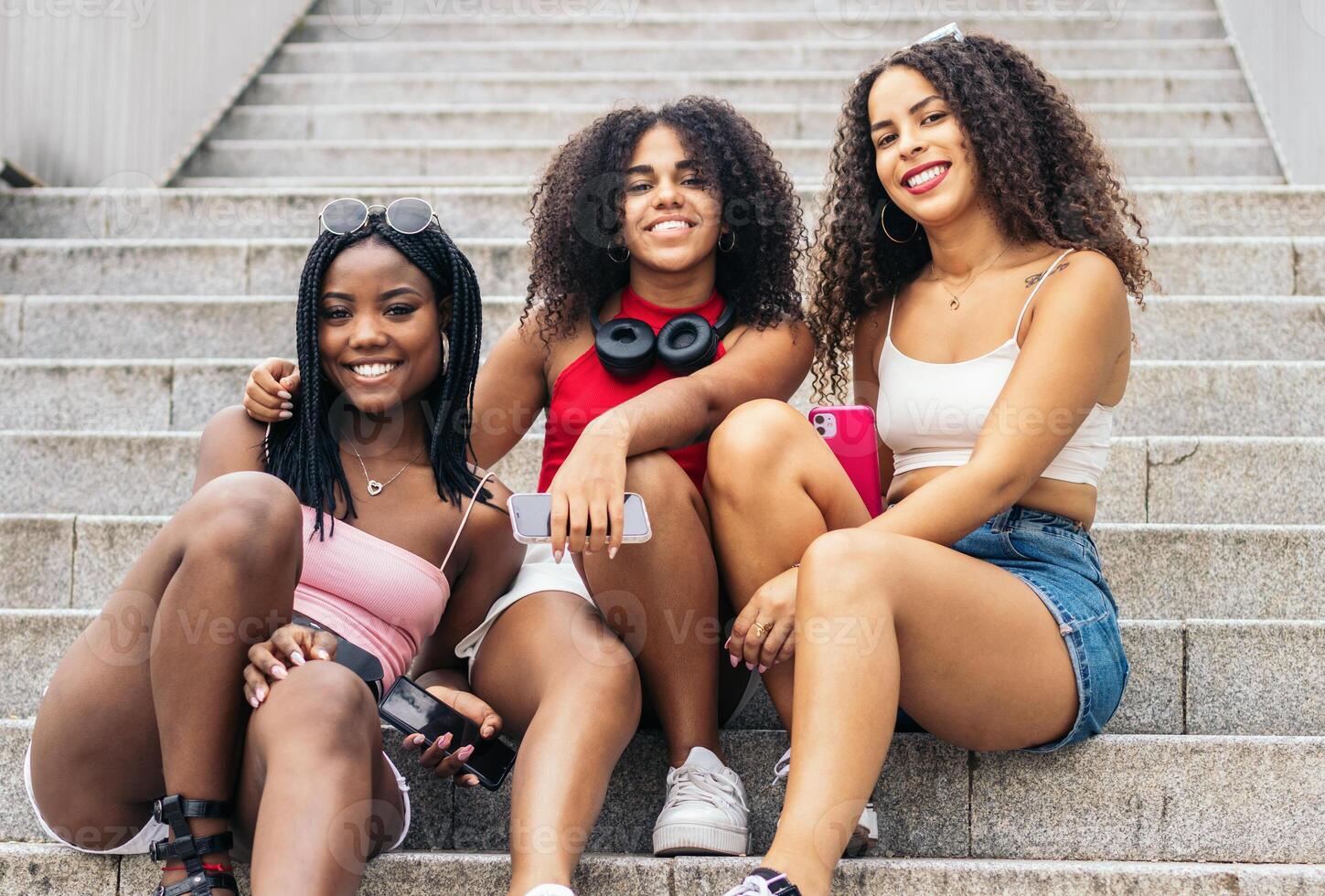 Tres joven mujer sentado en pasos con auriculares en el cuello foto