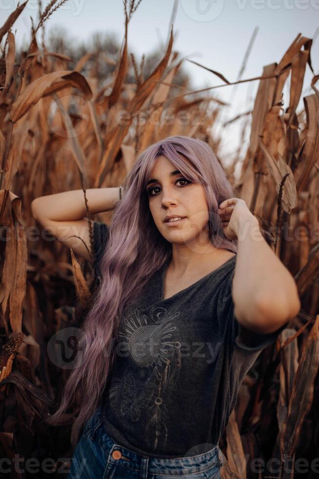 A woman with purple hair standing in a corn field looking at the camera photo