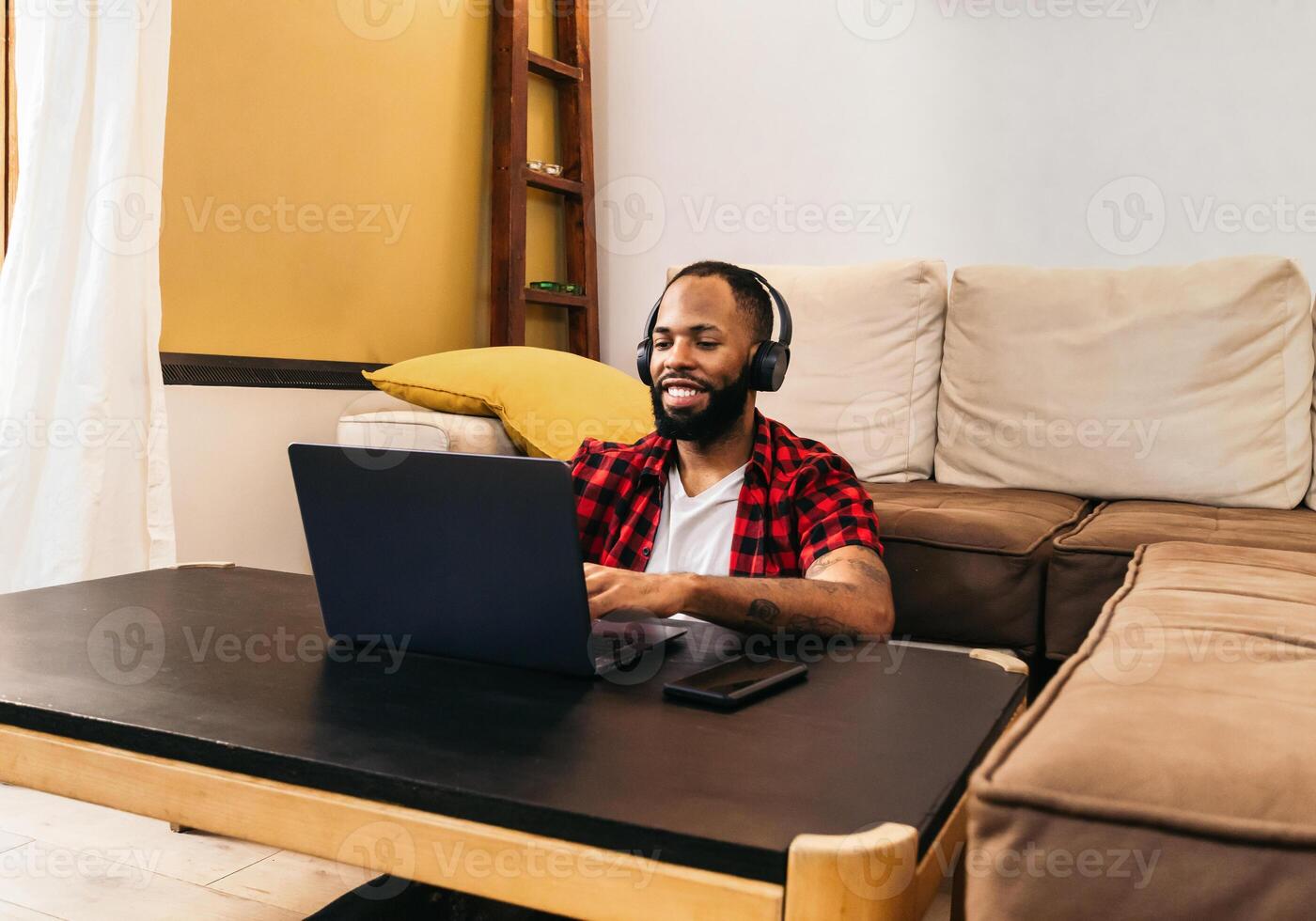 A man with headphones sitting on a couch with a laptop to work on photo