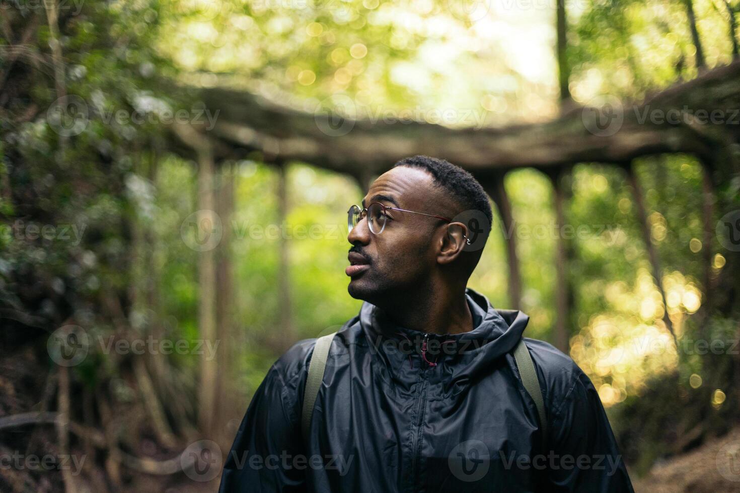 A man in a black rain jacket standing in the woods while looking away photo