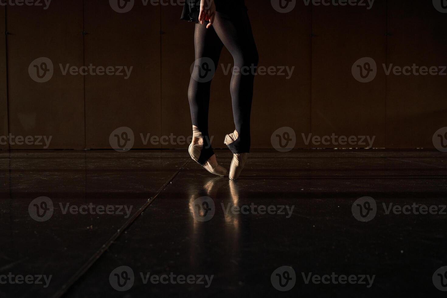A woman in black tights and pointe shoes is standing on a black floor photo
