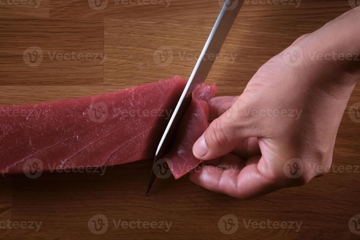 A person carefully cutting a piece of raw meat with a knife photo