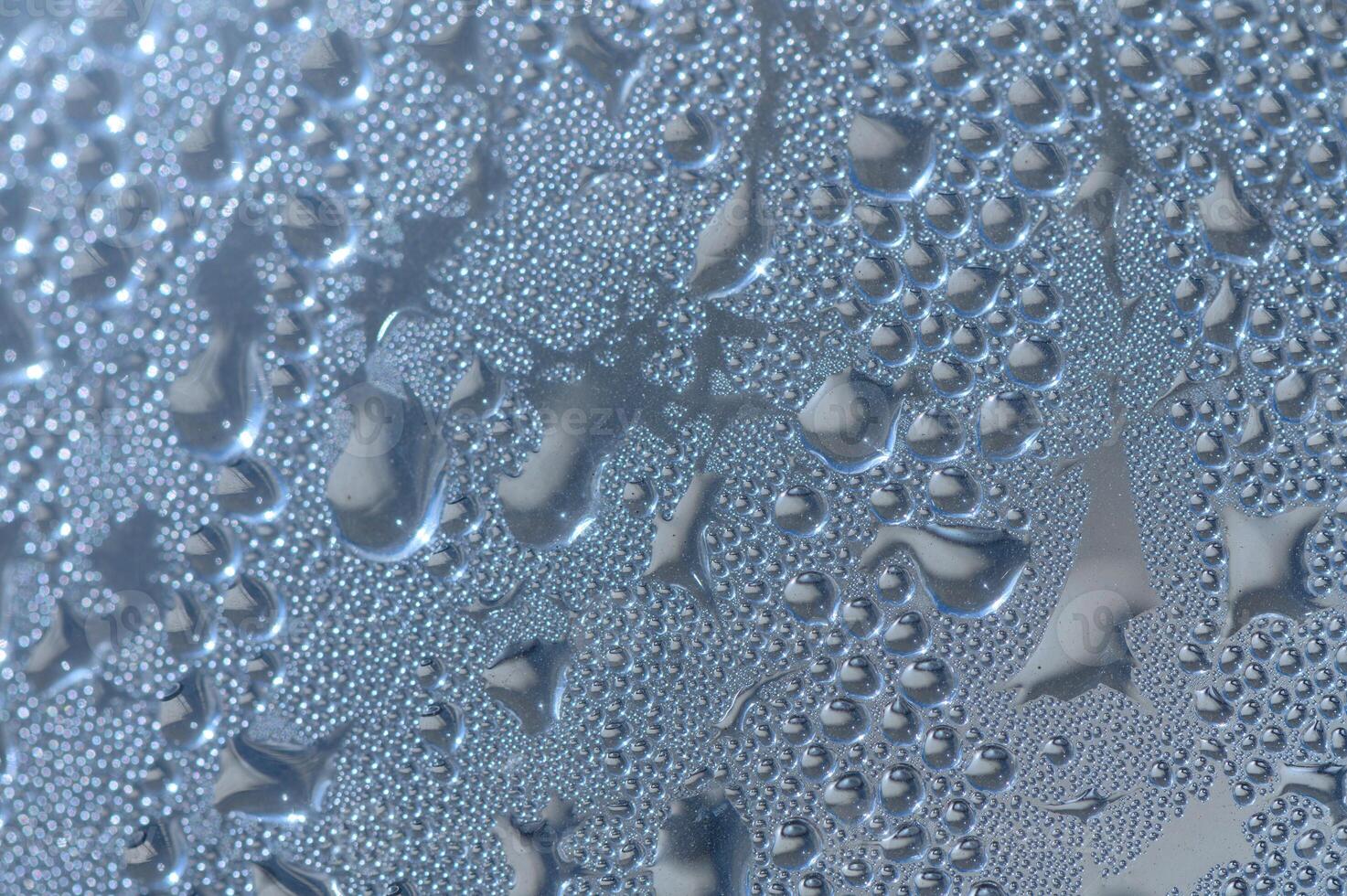 Raindrops dance on a window glass, creating a mesmerizing pattern under soft indoor lighting photo