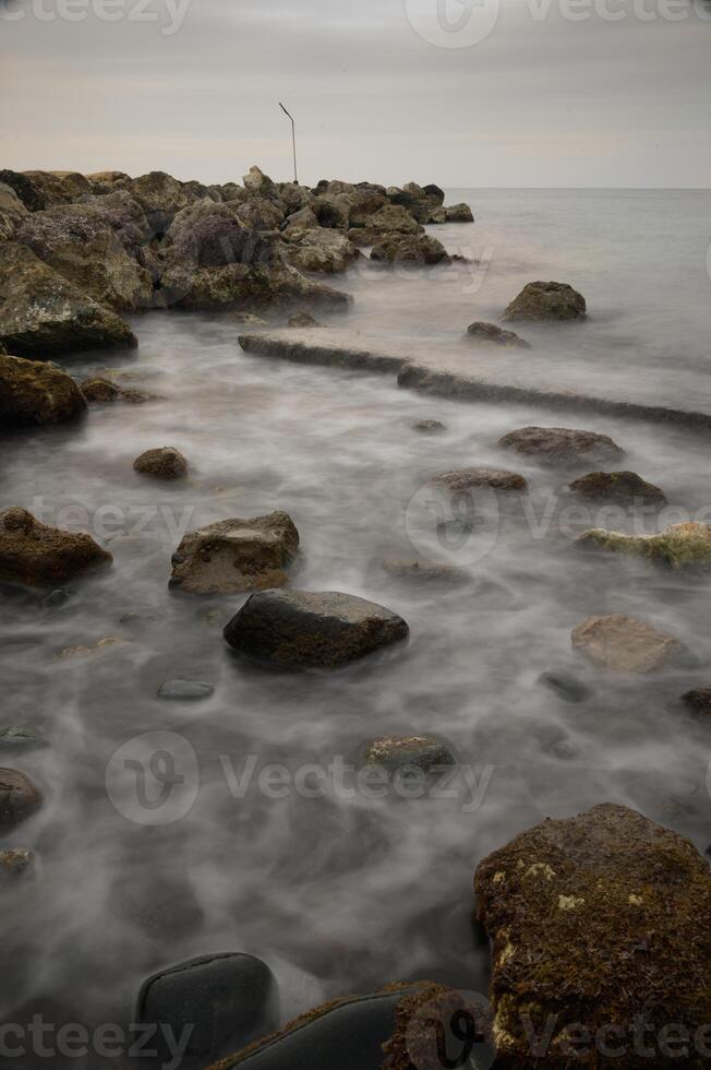 Calm waters dance with mist over rocky shoreline at dusk by the tranquil coast photo