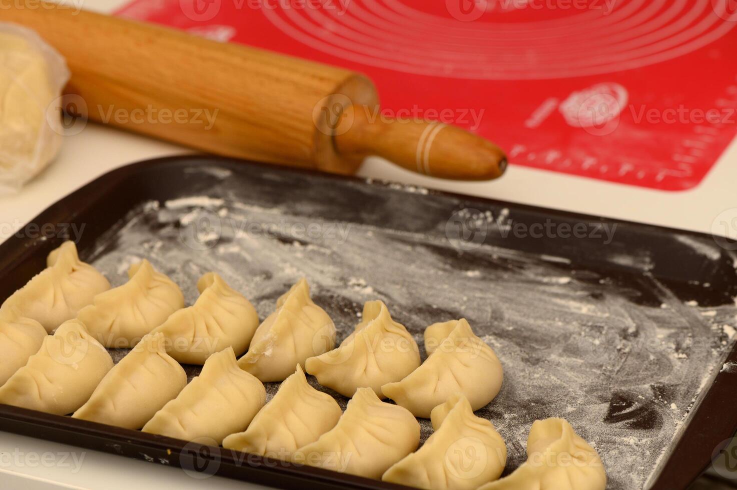 Homemade dumplings arranged neatly on a baking tray with a rolling pin in a cozy kitchen setting photo