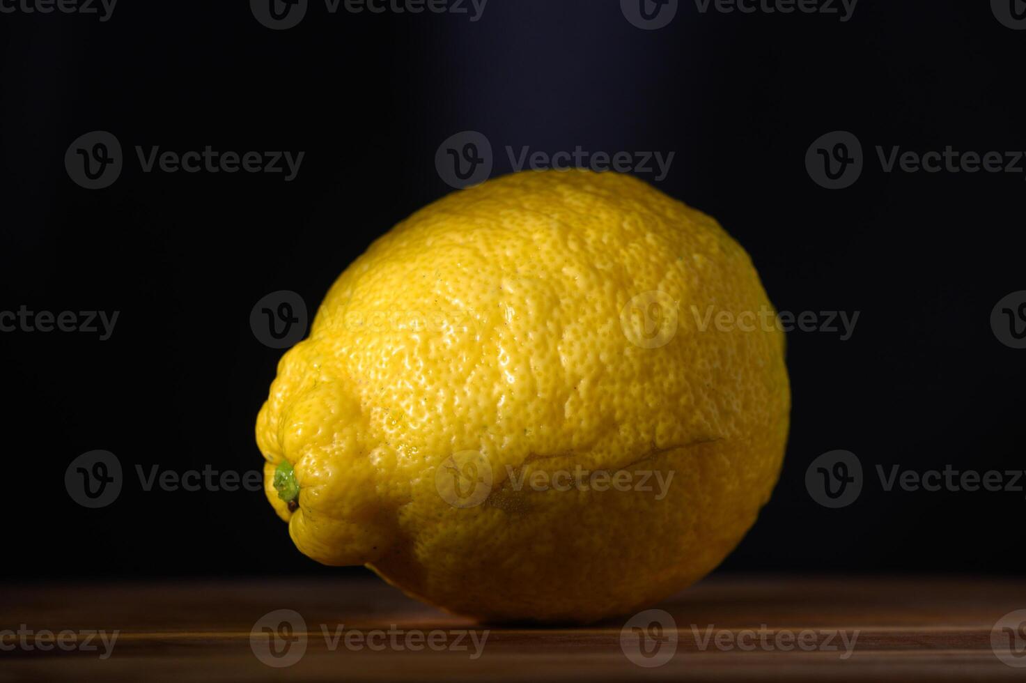 Bright yellow lemon glows softly against dark backdrop on a wooden surface photo