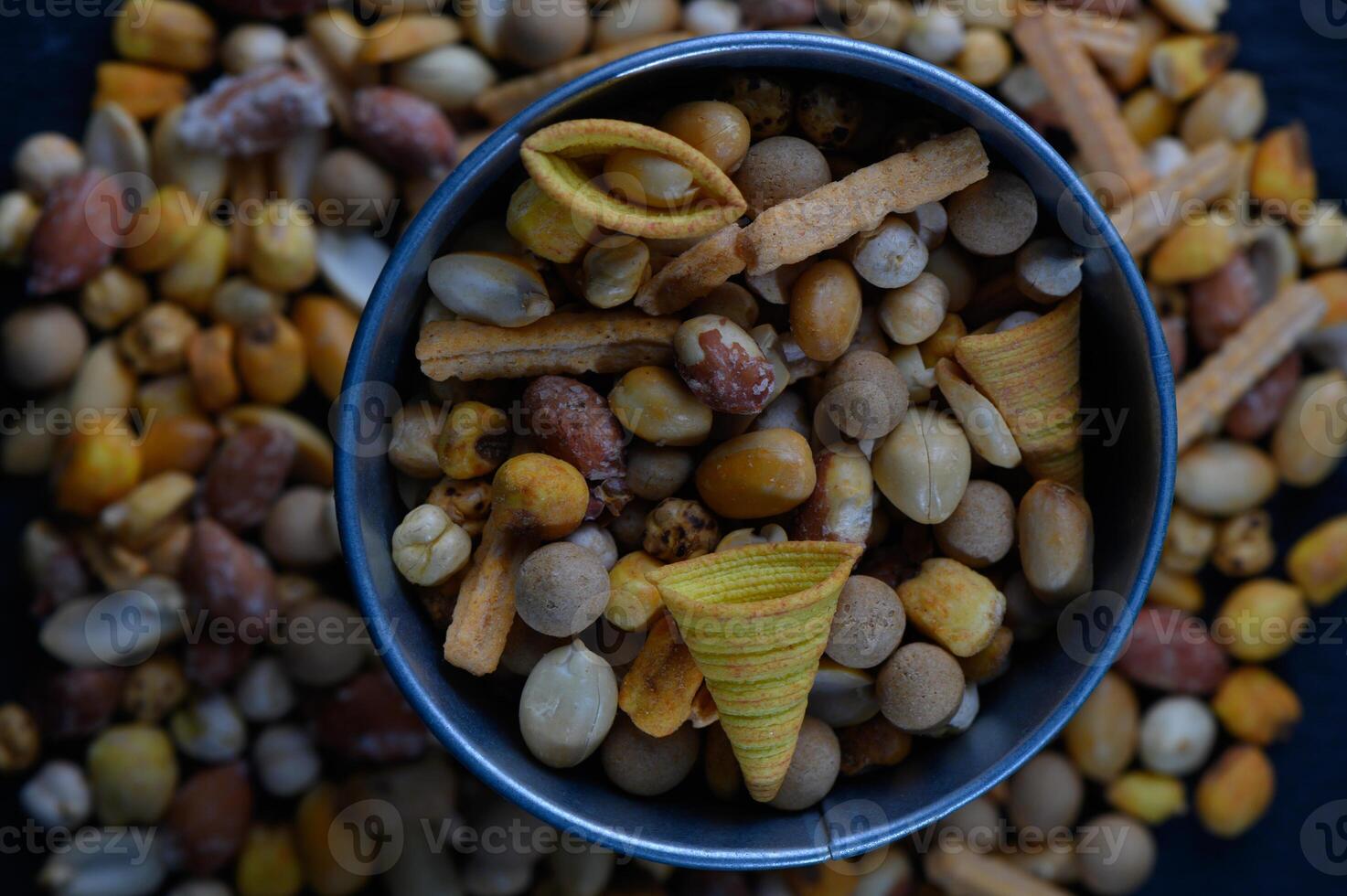 Colorful assortment of crunchy snacks in a bowl decorated with various nuts and flavors on a dark surface photo
