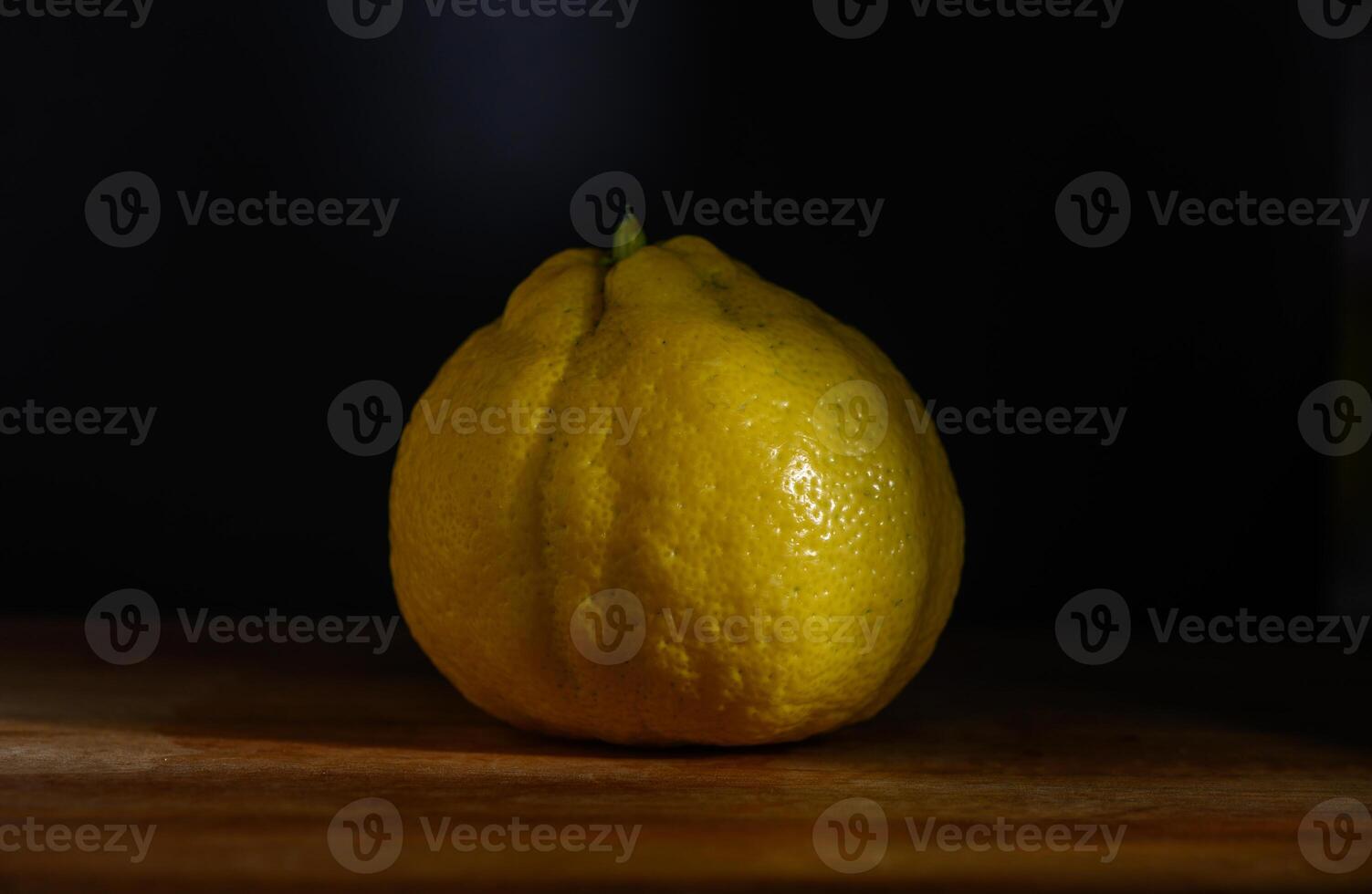 Unique yellow lemon rests on wooden surface under soft lighting in an artistic still life composition photo
