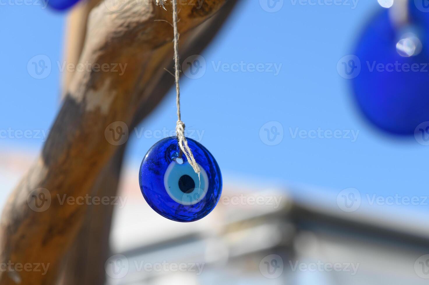 Bright blue glass talisman catches sunlight while hanging from a twisted branch against a clear sky photo