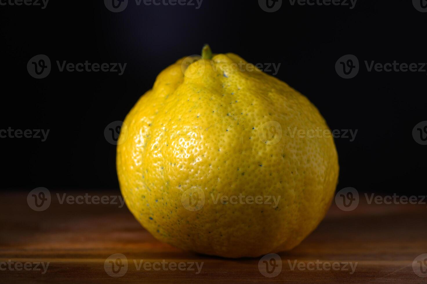 Vibrant yellow citrus fruit showcases unique texture and shape against dark background photo
