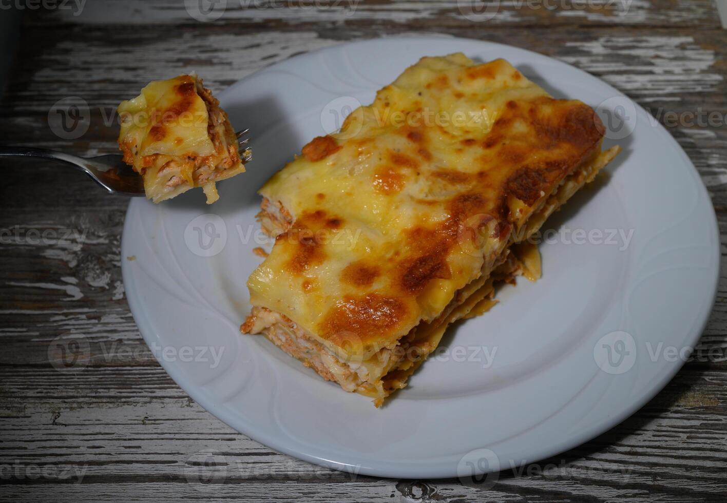 Delightful layers of cheesy chicken lasagna served on a rustic wooden table at sunset photo