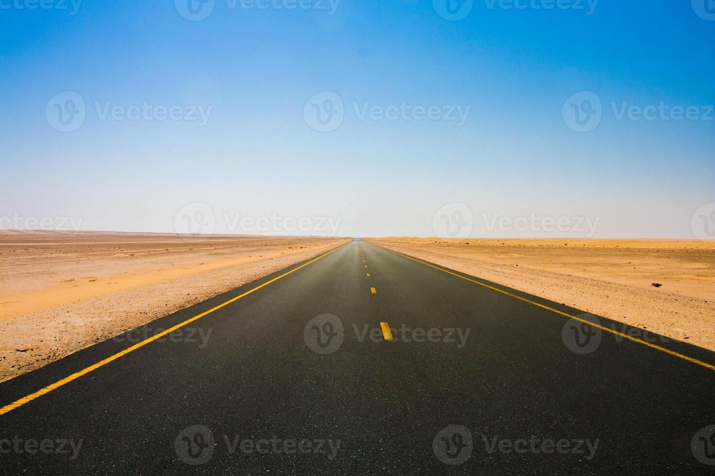An empty road in the desert with a blue sky photo