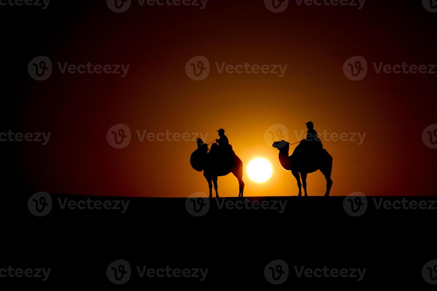Two people on camels are silhouetted against the setting sun photo
