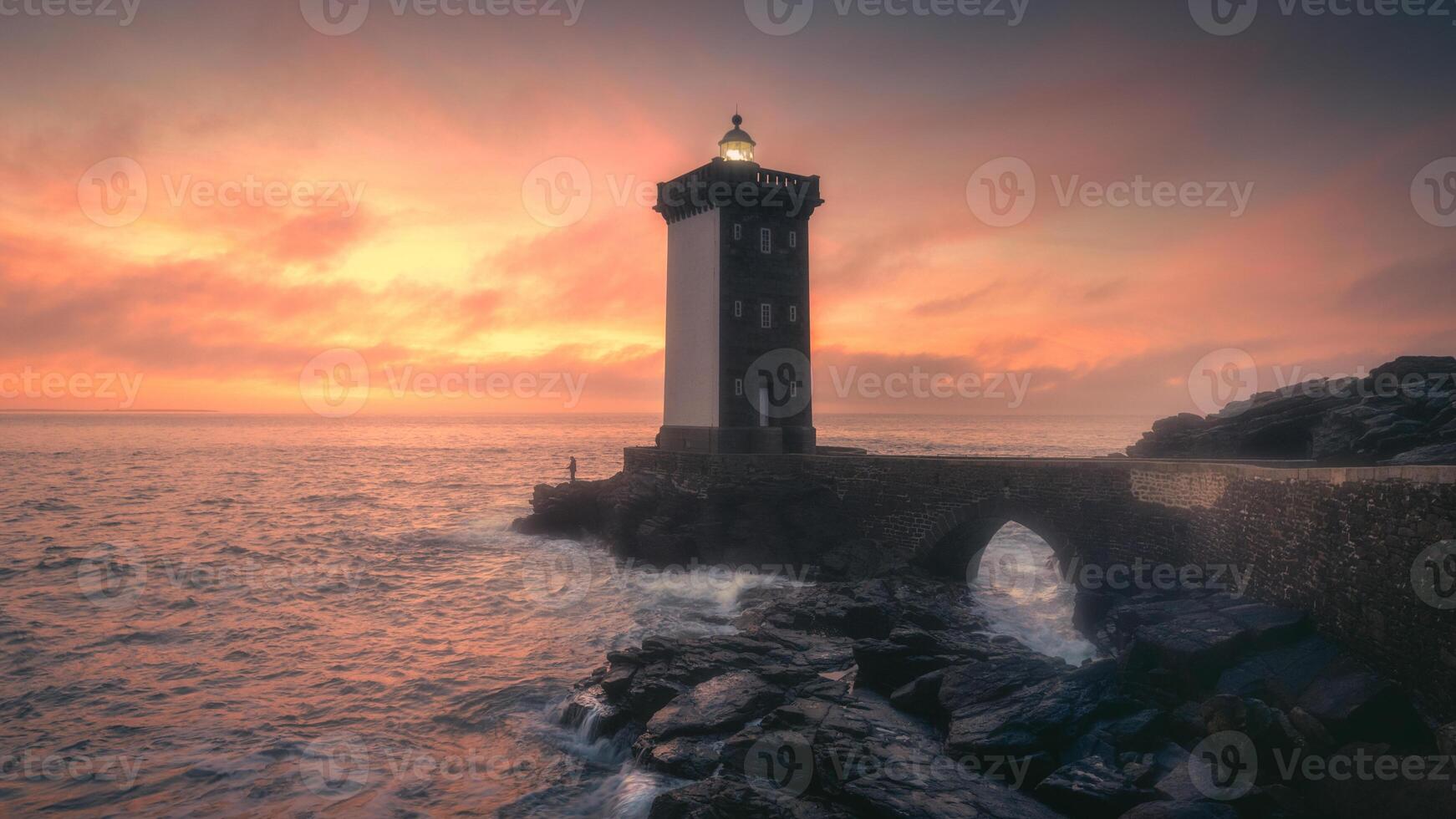 A lighthouse stands on the shore of the ocean at sunset photo