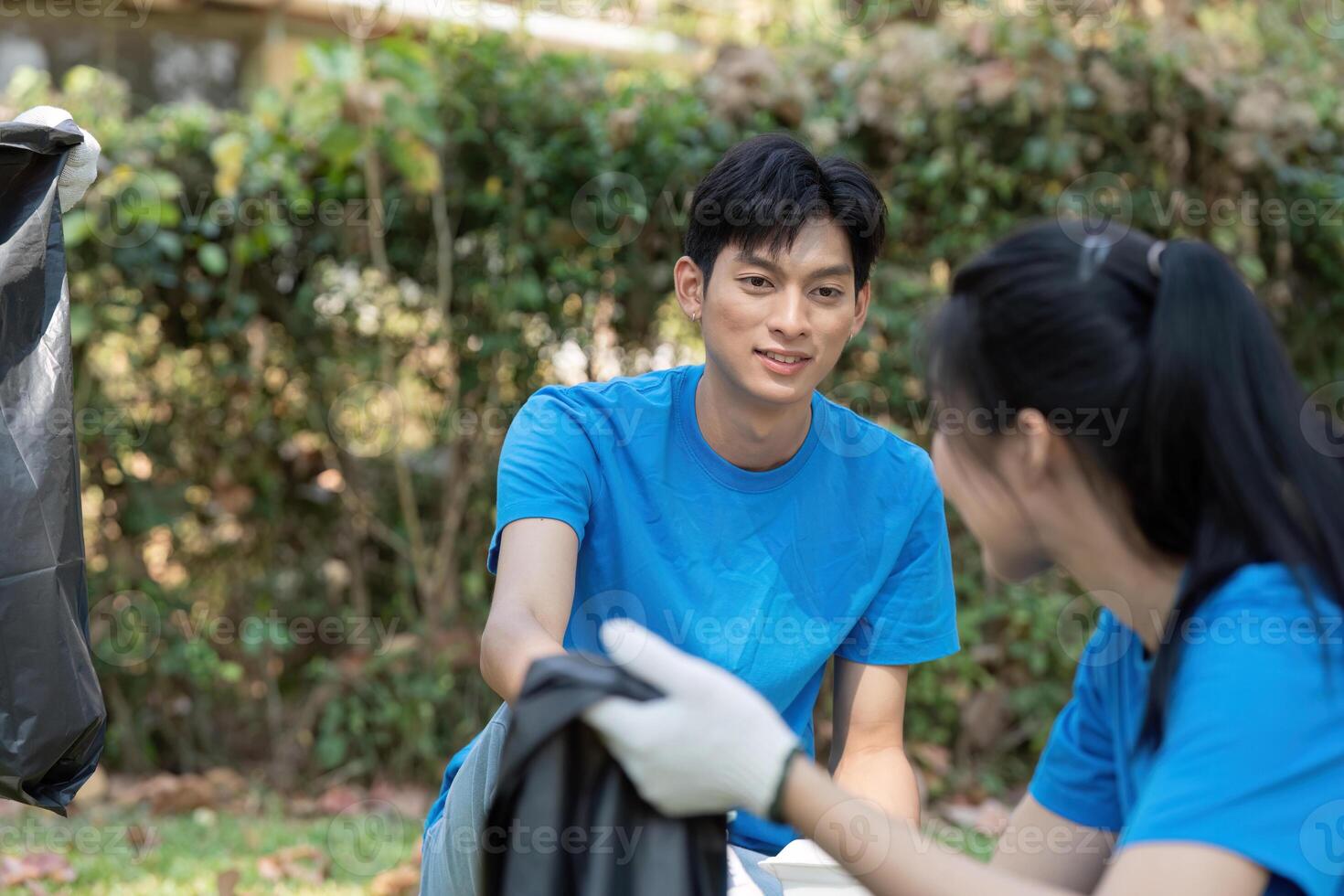 Volunteerism and Sustainability. A young volunteer enthusiastically engages with a fellow volunteer while picking up litter in a park. photo