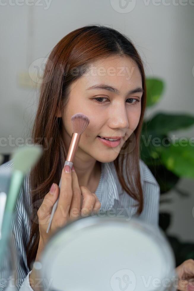 Beauty and Makeup Application. A woman applying blush with a brush while looking into a mirror, showcasing her radiant smile. photo