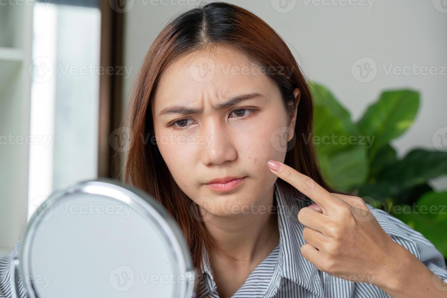 Skin Concerns and Self-Reflection. A woman examines her skin in the mirror, addressing skincare issues with concern. photo