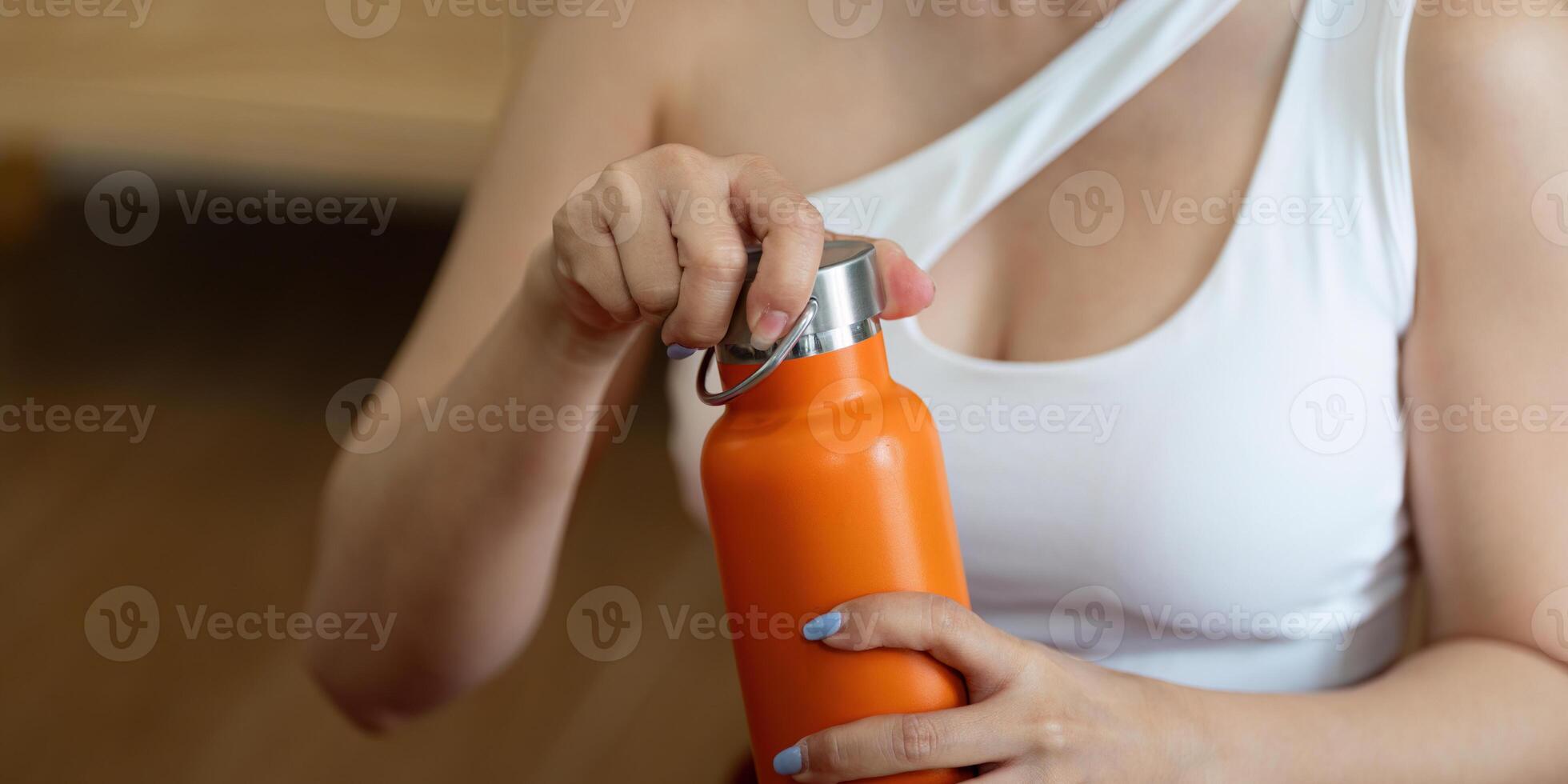 Hydration and Wellness. A woman opening a bright orange water bottle after her workout session to stay refreshed. photo