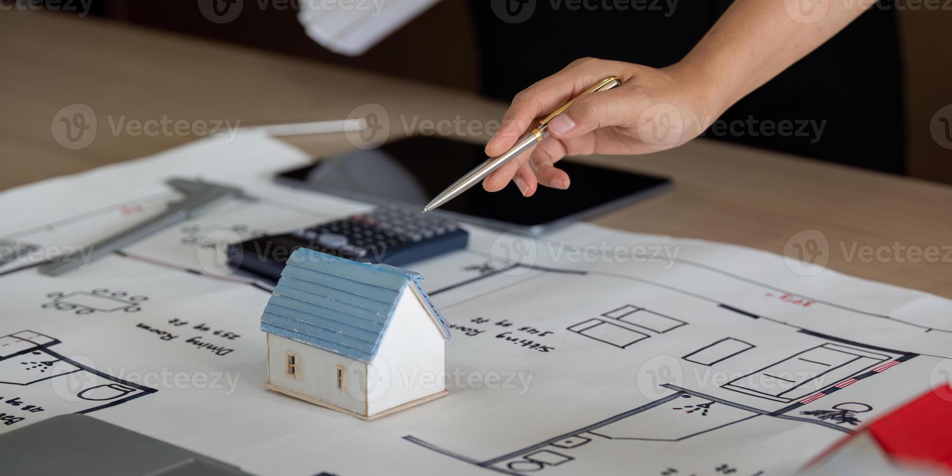 Model Building and Project Planning. A hand points to a miniature house on a blueprint, illustrating home construction planning. photo