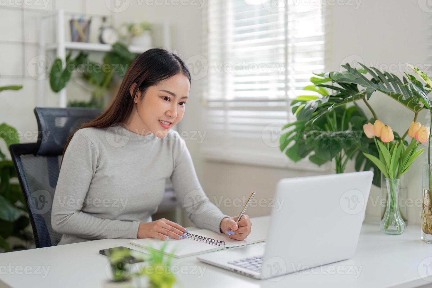 Focus and Engagement. A woman takes notes while attending an online meeting. photo