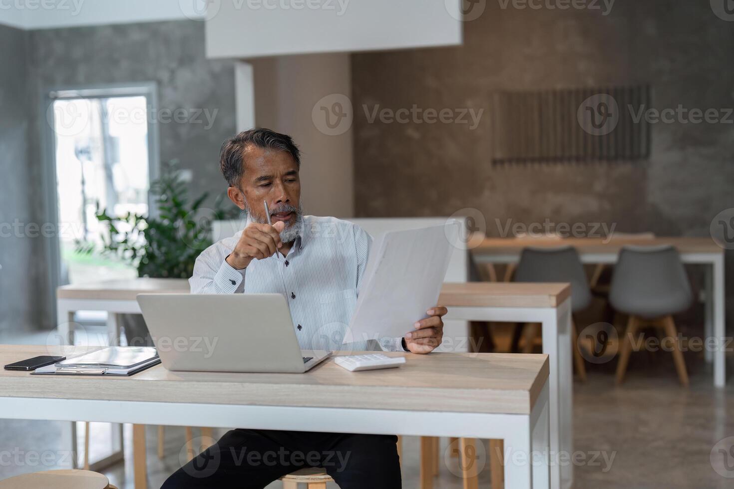 Insightful Review and Business Strategy. A senior male professional analyzing documents and digital information at his desk. photo