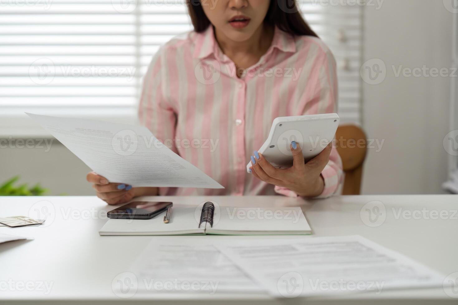 Home Office and Financial Stress. A woman managing her finances at her home office, looking concerned while reviewing documents and using a calculator. photo