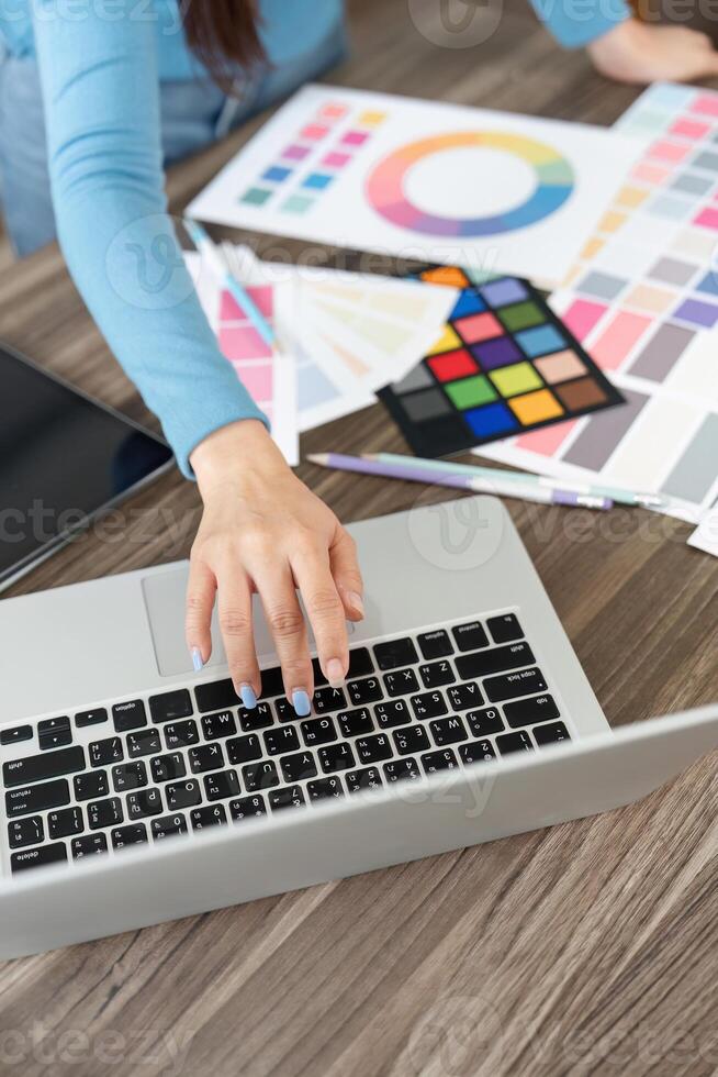 Digital Design and Collaboration. A designer types on a laptop while surrounded by colorful design materials and palettes. photo