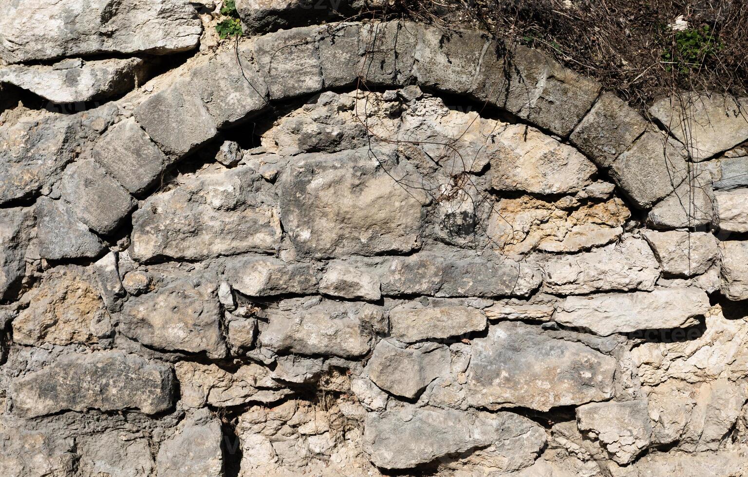 An ancient stone wall with archway provides a textured and historical architectural background. photo