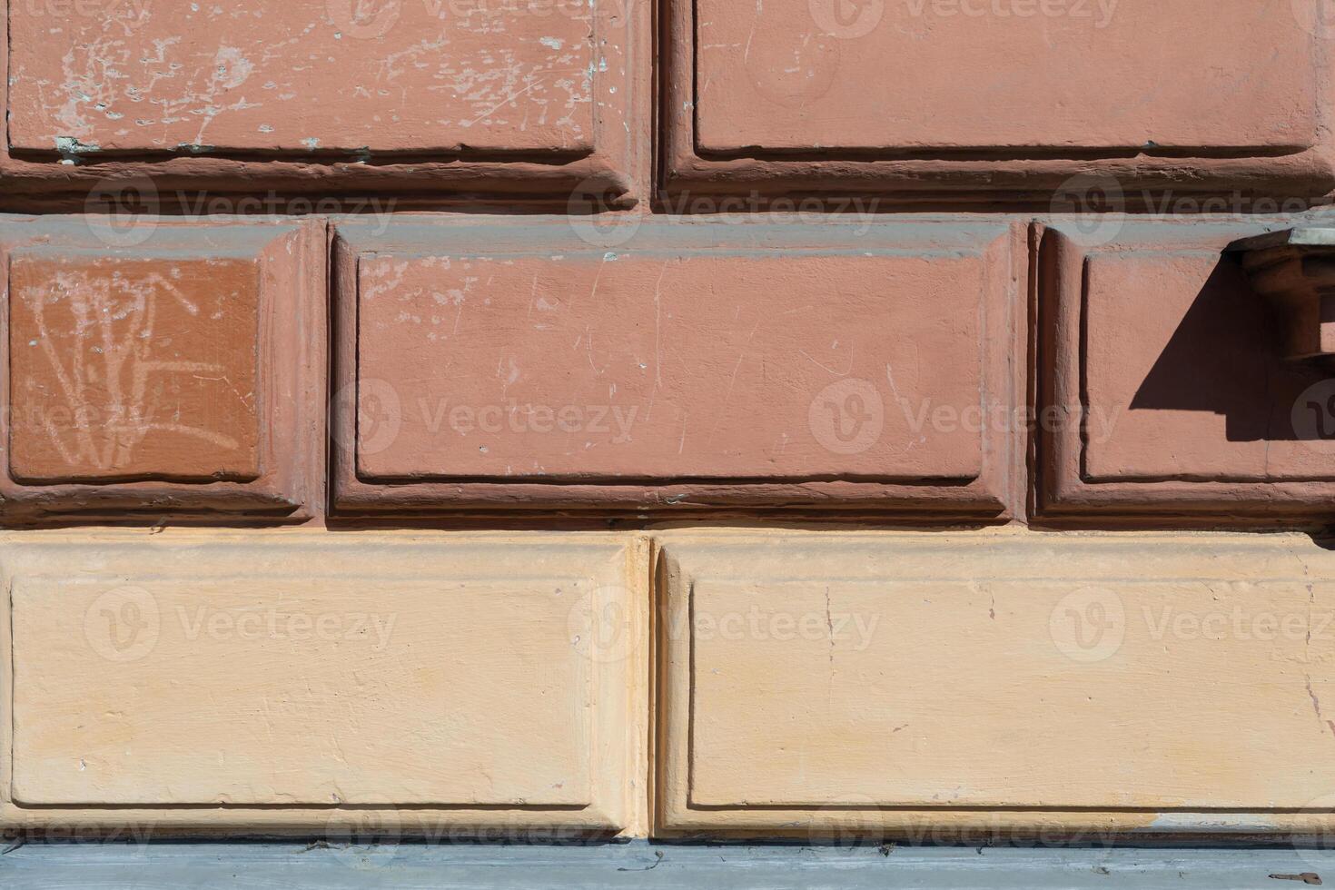 An aged building exterior showcases a textured two-tone wall with architectural detailing, casting subtle shadows. photo