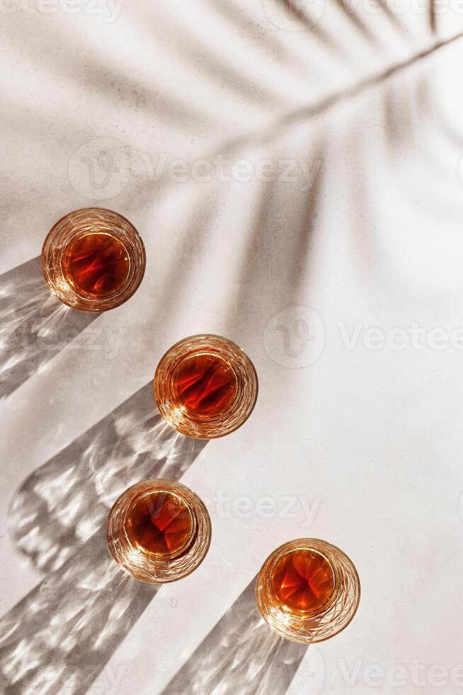Whiskey Glasses with palm leaf Shadows and sunlight Reflection on beige background, glass with strong alcohol, aesthetic top view summer still life, refraction at crystal shine cups, caustics photo
