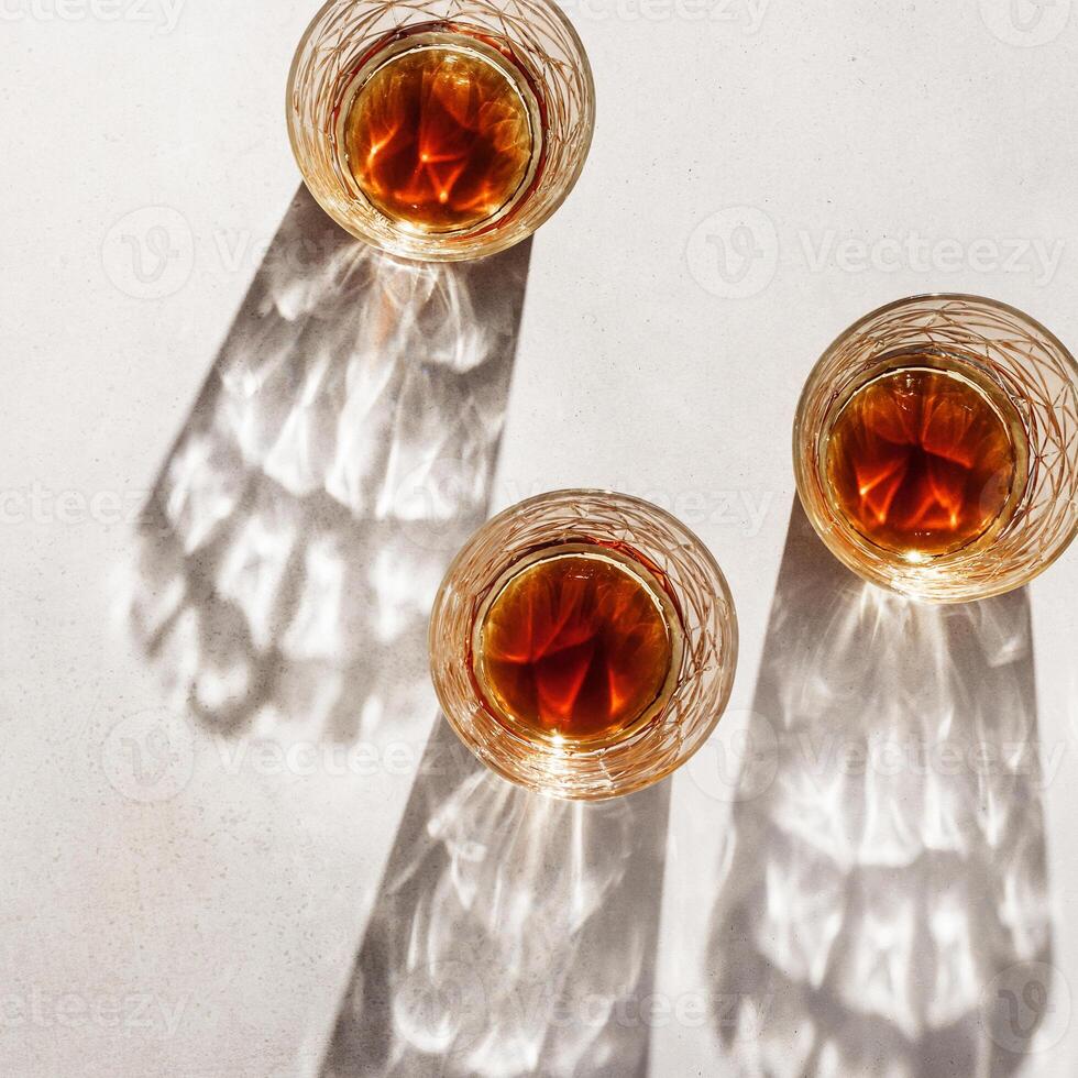 Transparent alcohol Glasses with dark shadows at sunlight on beige texture table, top view minimal style, aesthetic flat lay shiny glass sparkling at natural light, summer strong drink, card photo