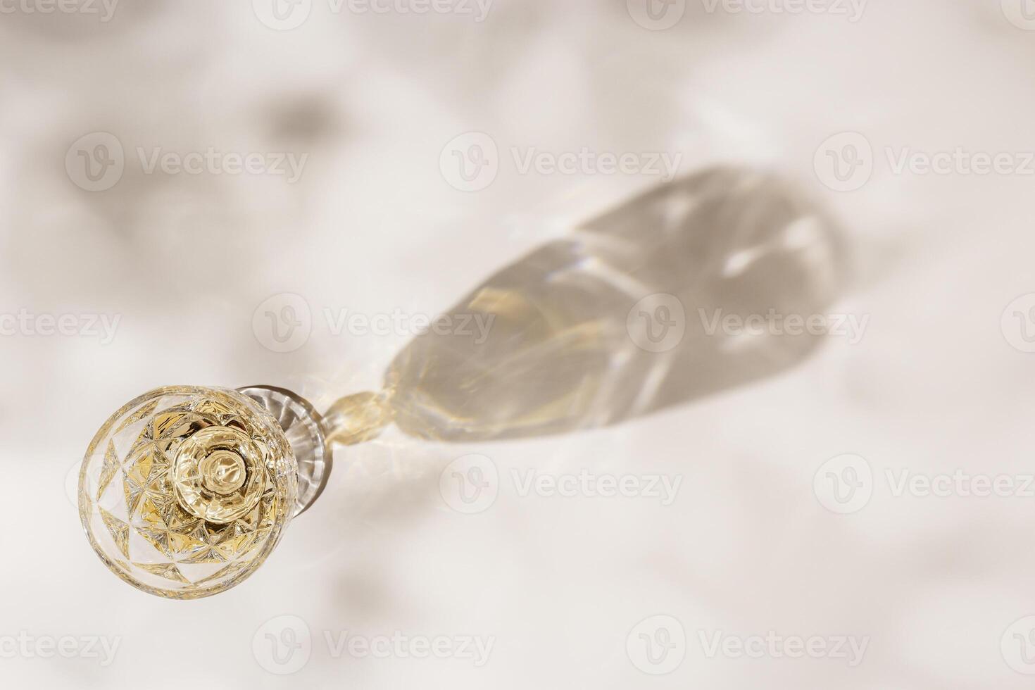 White wine in crystal transparent fashion glass with leaves shadow at sunlight, beige background and beautiful light, creative summer alcohol drink minimal concept, copyspace, top view photo