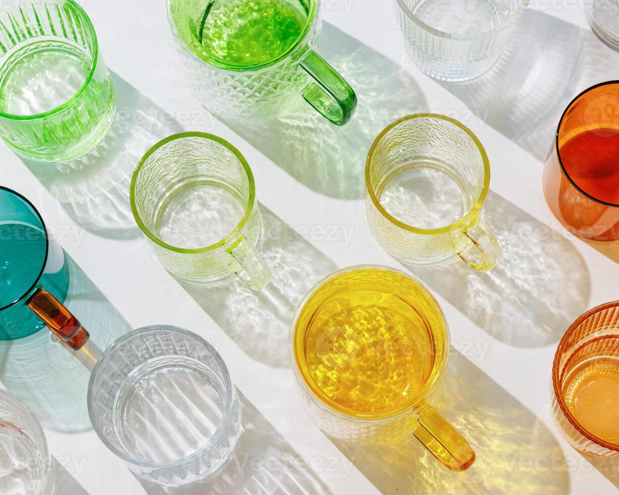 Colored shiny drink Glasses still life with shadow and sunlight reflections on white, minimal aesthetic top view summer photo, refraction at glass cups with sun flare, creative modern pattern photo