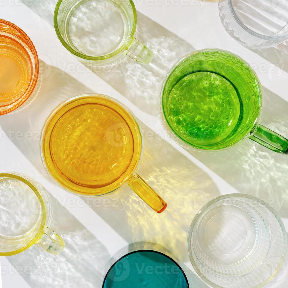 Colored shiny drink Glasses still life with shadow and sunlight reflections on white, minimal aesthetic top view summer photo, refraction at glass cups with sun flare, creative food pattern photo