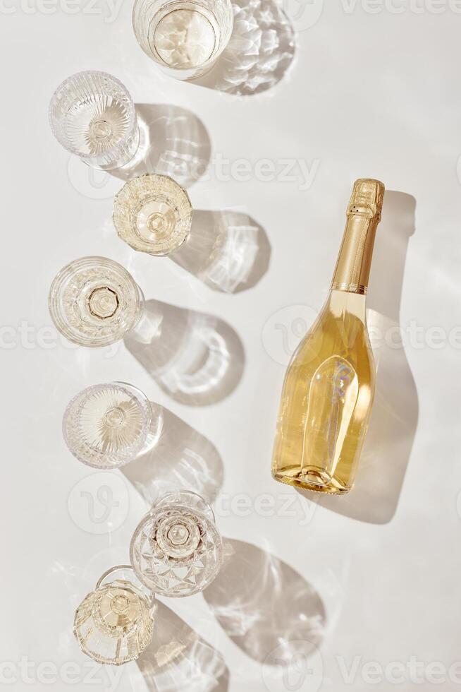 Summer party drinks flat lay, wine glasses with white sparkling wine and sunshine shadow on light table. Minimal pattern with beautiful wine glasses, above view still life, beige golden colored photo