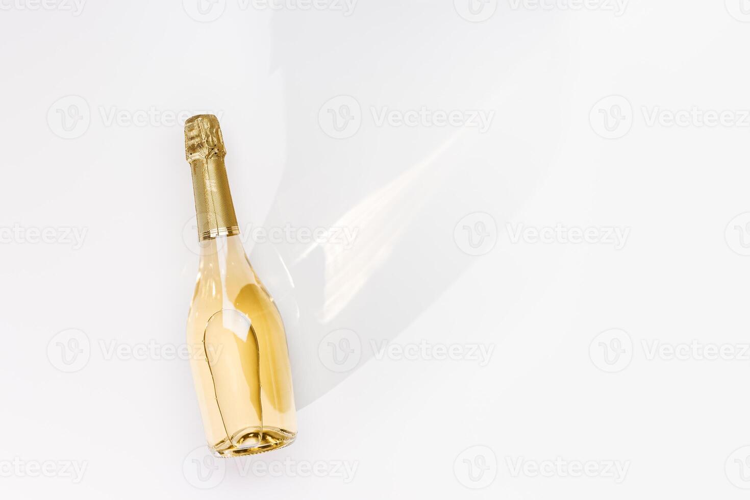 Top view white sparkling wine bottle with sunshine long shadow and flare on light white background. Minimal aesthetic flat lay, one champagne bottle with golden. Summer alcohol drink photo